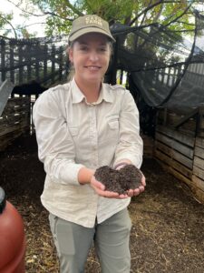 Farm team member Katie smiles as she holds out rich compost in her two hands. 